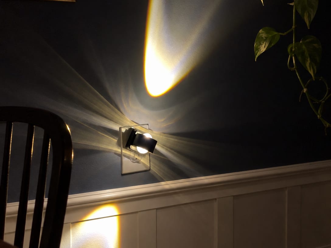 Aoraglow glowing warm against a navy wall at night, true to its size beside the outlet plate, the room calm and dim like a
