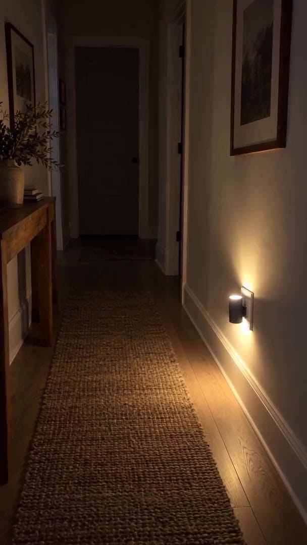 Aoralight - Home Glow Kit glowing soft amber low on a kitchen wall at night, small beside the outlet plate, a warm pool of